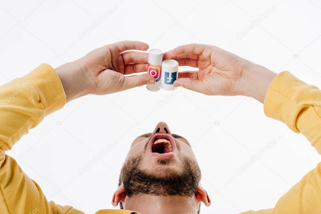 Young man imitating using pills from container with facebook and instagram logos isolated on white