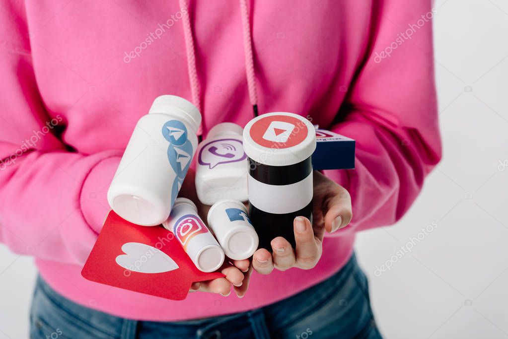 Cropped view of girl holding containers with social media logos and red paper cut card with heart symbol isolated on grey