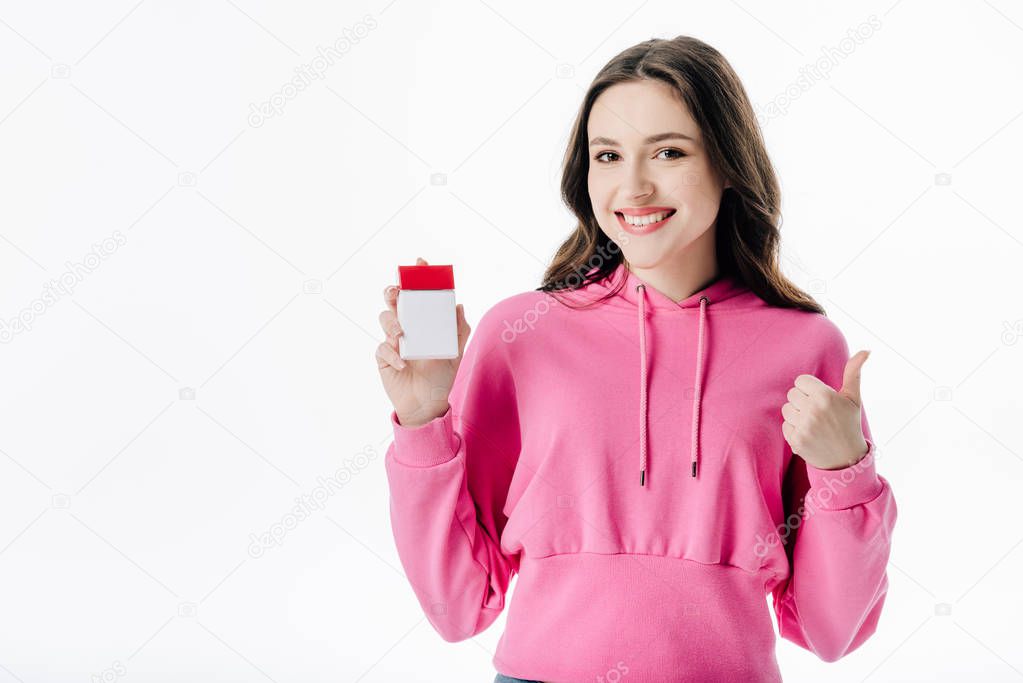 cheerful young girl holding cigarette pack and showing thumb up isolated on white