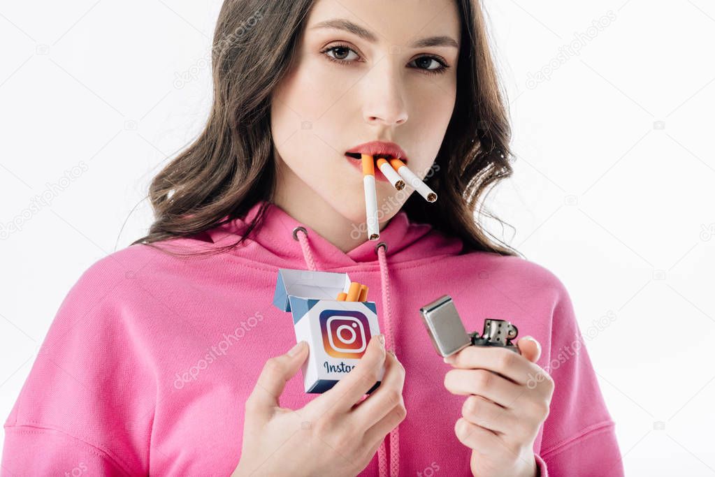 Young girl with cigarettes in mouth holding cigarette pack with instagram logo isolated on white