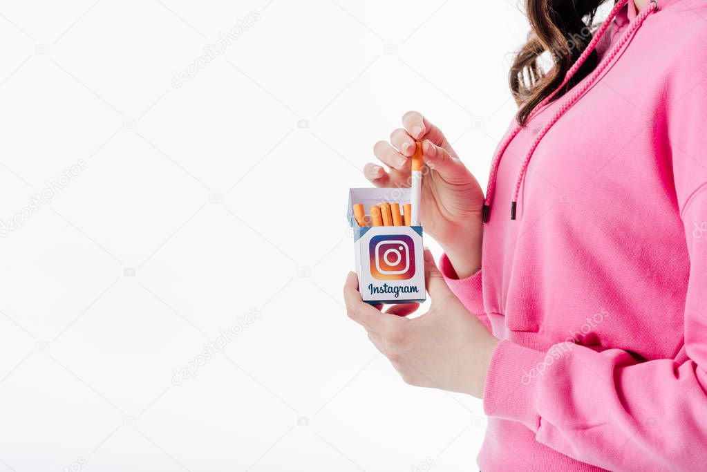 Cropped view of young girl holding cigarette pack with instagram logo isolated on white