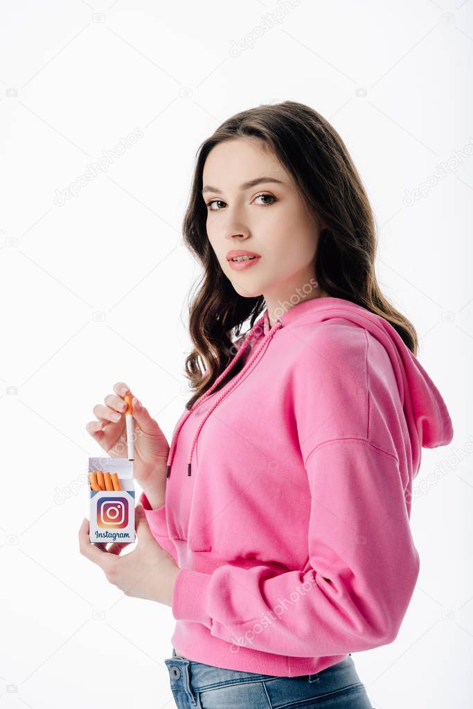Beautiful young girl holding cigarette pack with instagram logo and looking at camera isolated on white