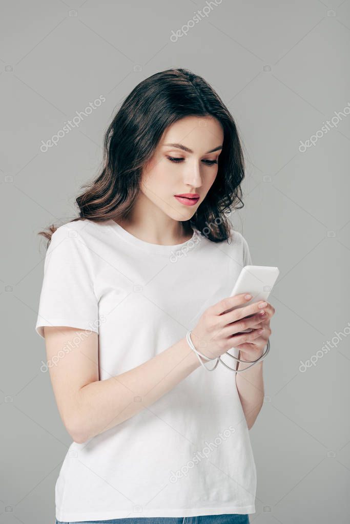 concentrated young girl in white t-shirt using smartphone isolated on grey