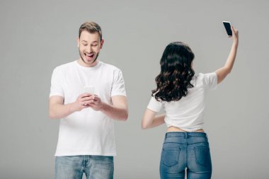 gri izole selfie çekerken kızın yanında dururken akıllı telefon kullanan heyecanlı genç adam 