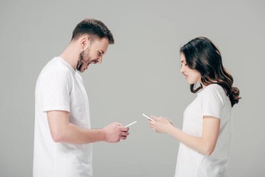 yakışıklı adam akıllı telefon kullanarak ve gri izole akıllı telefon ile hoşnutsuz kız yakınında dururken bağırıyor