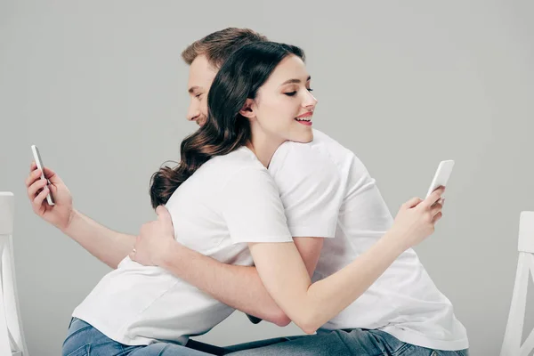 Joven Hombre Mujer Abrazándose Mientras Usa Teléfonos Inteligentes Aislados Gris —  Fotos de Stock