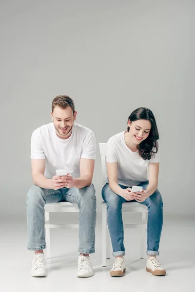 Young Smiling Man Woman Sitting Chairs Using Smartphones Grey Background — 스톡 사진