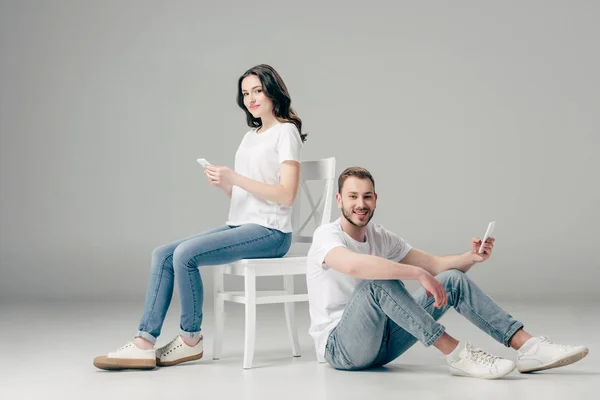 Mujer Sonriente Usando Teléfono Inteligente Cerca Hombre Alegre Sentado Suelo — Foto de Stock