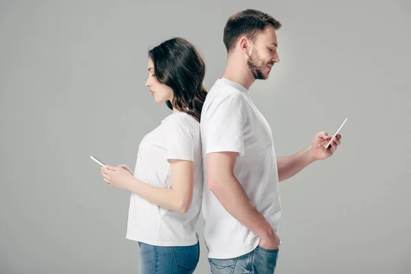 티셔츠를 남녀가 돌아가 회색으로 고립된 스마트폰을 사용한다 — 스톡 사진