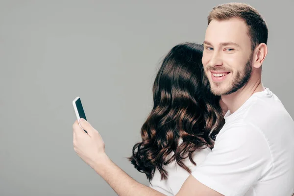 Hombre Sonriente Guapo Abrazar Mujer Uso Teléfono Inteligente Aislado Gris — Foto de Stock