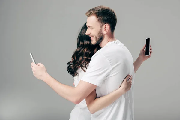 Young Couple White Shirts Hugging While Using Smartphones Grey Background — 스톡 사진