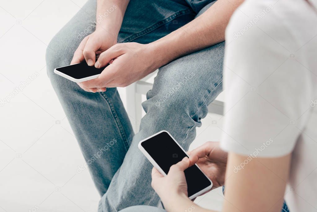 partial view of man and woman in blue jeans using smartphones isolated on white