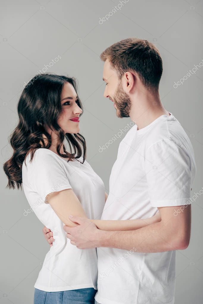 happy young couple embracing and looking at each other isolated on grey