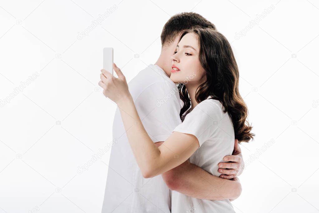 pretty young girl using smartphone while embracing with boyfriend isolated on white