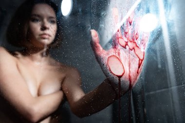 selective focus of naked girl with bleeding hand touching glass in bathroom clipart