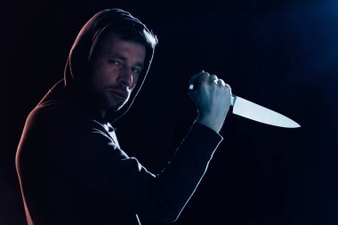 criminal in casual clothes holding knife and looking at camera on black clipart