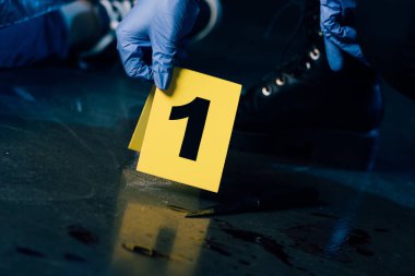 partial view of investigator in rubber gloves with evidence marker at crime scene clipart