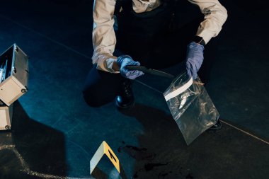 cropped view of investigator putting knife in ziploc bag at crime scene clipart
