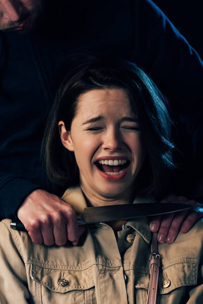 partial view of criminal attacking woman with knife isolated on black