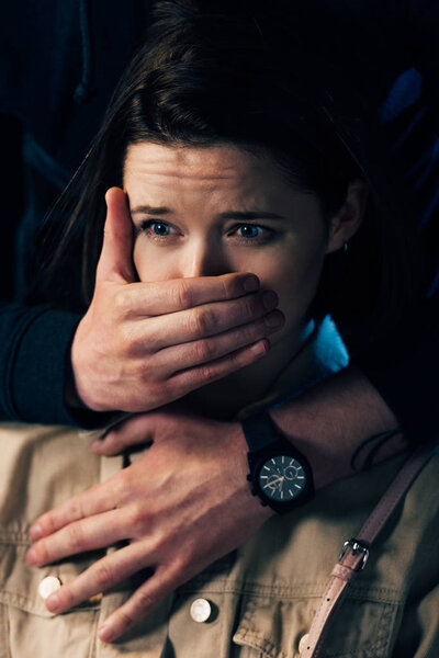 partial view of criminal attacking scared woman and covering her mouth isolated on black