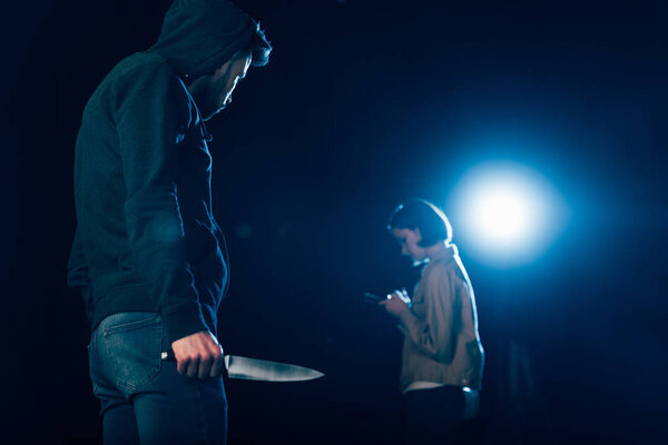 killer in hood holding knife and looking at woman on black