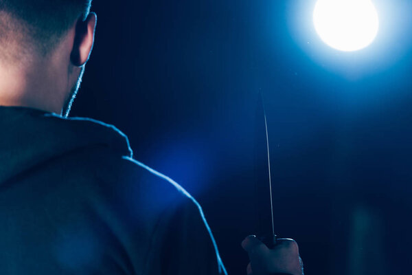 cropped view of killer holding knife on black