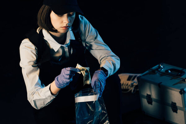 investigator in uniform putting dollar banknote in ziploc bag isolated on black