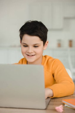 evde okul işi yaparken dizüstü bilgisayar kullanarak gülümseyen özenli çocuk