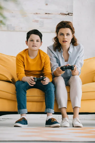 키예프 우크라이나 2019 노란색 소파에 앉아있는 조이스틱비디오 게임을 세심한 어머니와 — 스톡 사진