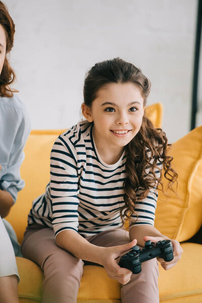 KYIV, UKRAINE - APRIL 8, 2019: Partial view of woman sitting near adorable child playing video game with joystick