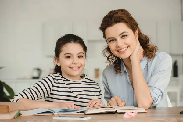 Beautiful Woman Adorable Smiling Daughter Looking Camera While Doing Homework — Stock Photo, Image