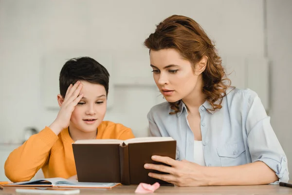 Bonita Mujer Con Lindo Hijo Leyendo Libro Mientras Hacen Trabajo — Foto de Stock