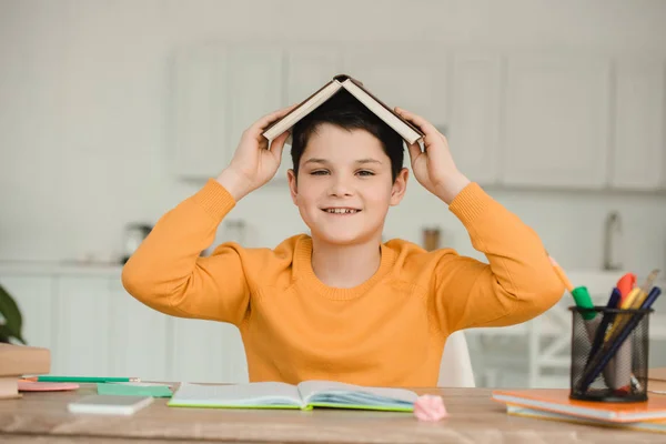 Glad Pojke Håller Öppen Bok Huvudet Och Tittar Kameran Medan — Stockfoto