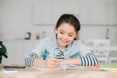 cute schoolchild writing in notebook while doing schoolwork at home clipart