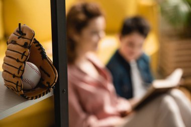 anne ve oğlu yere oturan ve birlikte kitap okuma yakın beyzbol eldiven ve top seçici odak