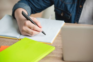 cropped view of schoolboy writing in notebook while doing schoolwork at home clipart