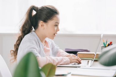 evde okul işi yaparken dizüstü bilgisayar kullanan sevimli çocuğun seçici odak