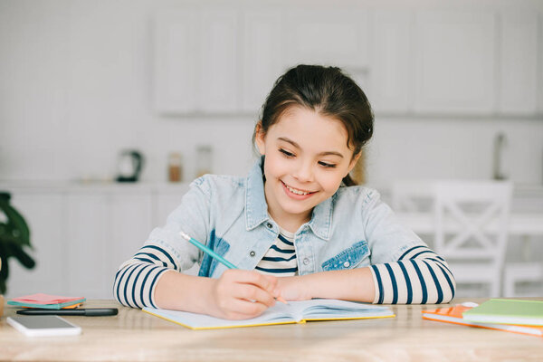 cute schoolchild writing in notebook while doing schoolwork at home