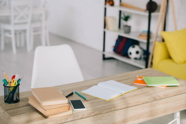 selective focus of wooden desk with books, stationery, copy books and smartphone with blank screen