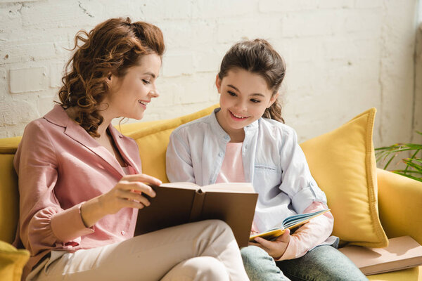 beautiful woman with adorable daughter reading book while doing homework together