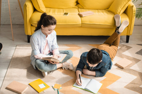 high angle view of adorable kids doing schoolwork on floor at home