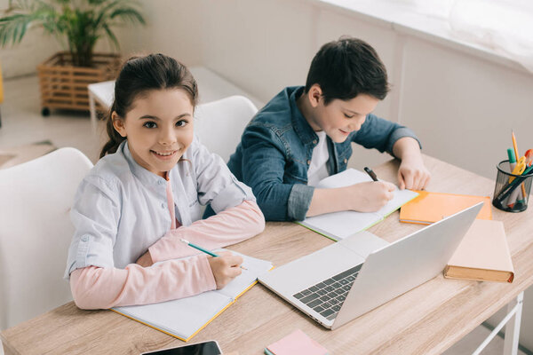 high angle view of cute brother and sister sitting at desk and doing homework together