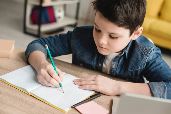 Bonito Atencioso Menino Escrever Notebook Enquanto Sentado Mesa Fazer Lição — Fotografia de Stock