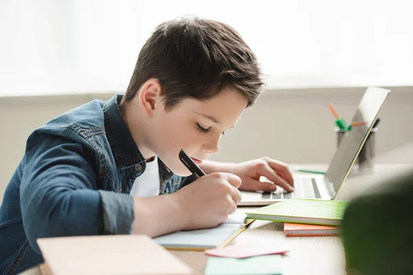 Adorable Attentive Boy Writing Notebook Using Laptop While Doing Homework — Stock Photo, Image