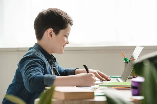 Smiling Boy Writing Notebook Using Laptop While Doing Schoolwork Home — Stock Photo, Image
