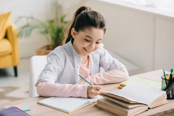 Αξιολάτρευτο Χαρούμενο Παιδί Γράφοντας Στο Σημειωματάριο Ενώ Κάθονται Στο Γραφείο — Φωτογραφία Αρχείου