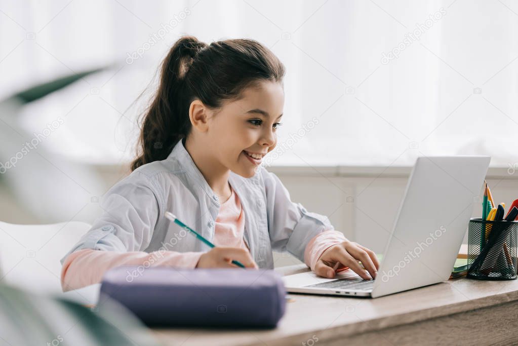 selective focus of cheerful child writing in notebook while doing homework