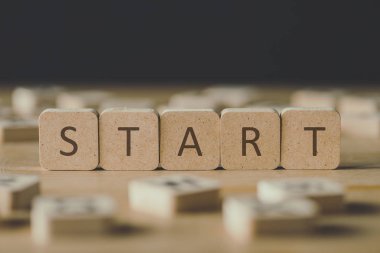 selective focus of start inscription on cubes surrounded by blocks with letters on wooden surface isolated on black clipart