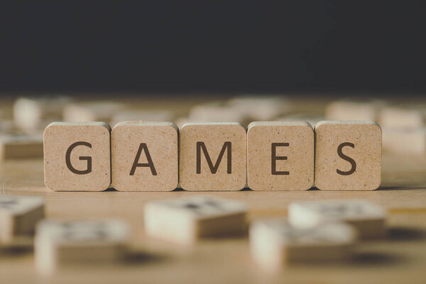 selective focus of cubes with word games surrounded by blocks with letters on wooden surface isolated on black
