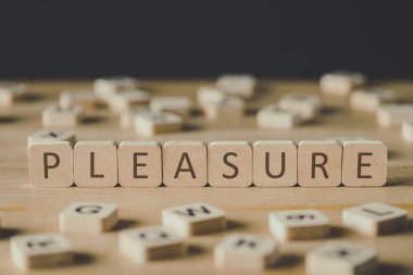 selective focus of pleasure lettering on cubes surrounded by blocks with letters on wooden surface isolated on black clipart